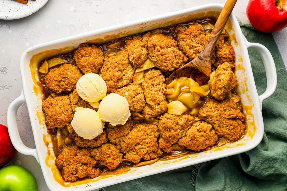 Apple cobbler with ice cream and fresh apples served in a baking dish.