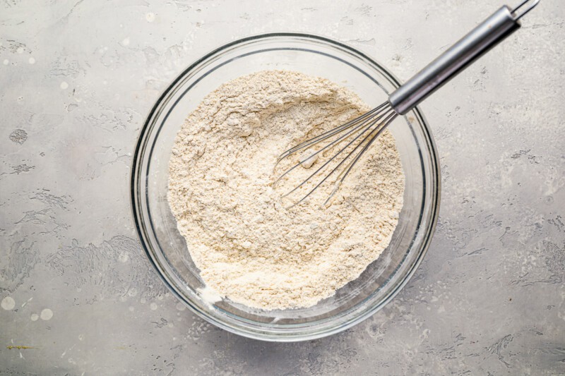 An apple cobbler filled with flour and a whisk.