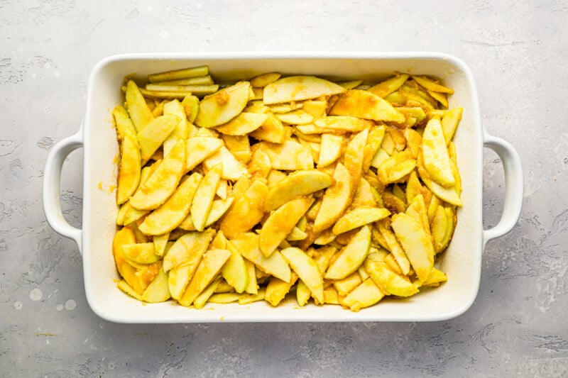 Apple cobbler with sliced apples in a white baking dish.