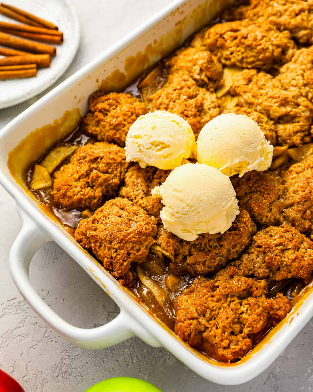 apple cobbler in a white baking dish, topped with scoops of vanilla ice cream.