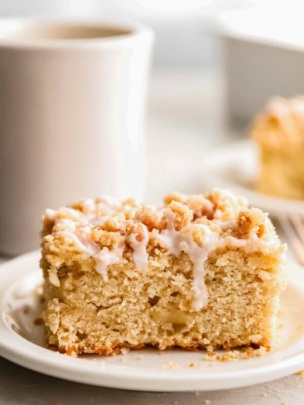 An irresistible apple coffee cake on a plate with a cup of steaming coffee.