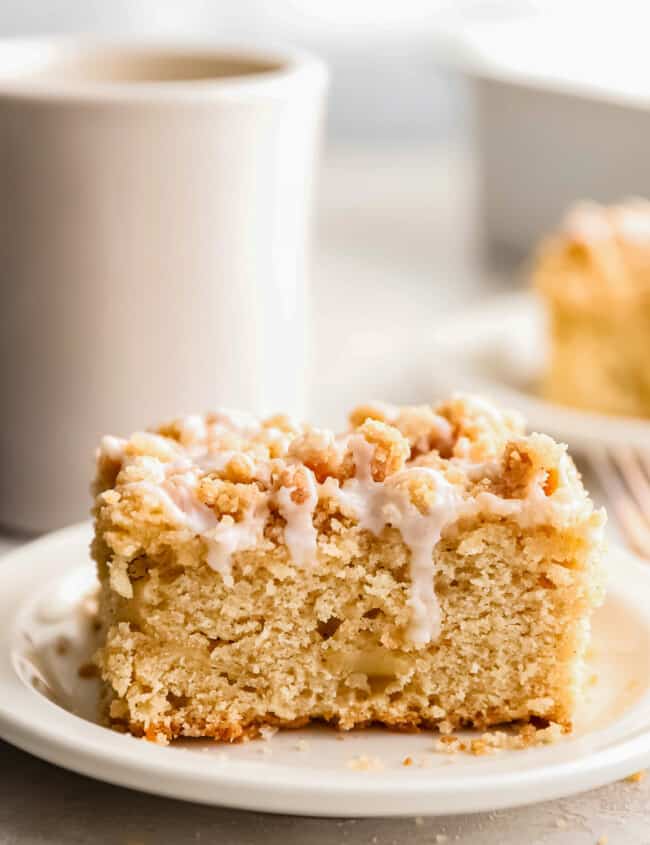 An irresistible apple coffee cake on a plate with a cup of steaming coffee.