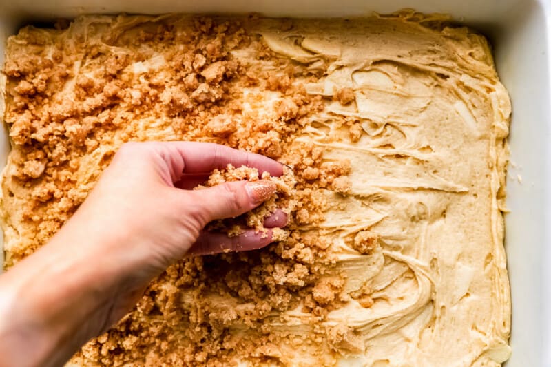 A hand grabbing a piece of crumb cake in a baking pan with apple coffee cake.