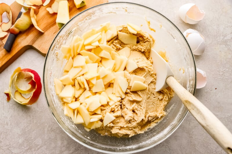 A bowl full of apples ready to be made into a delicious apple coffee cake, alongside a wooden spoon for mixing.