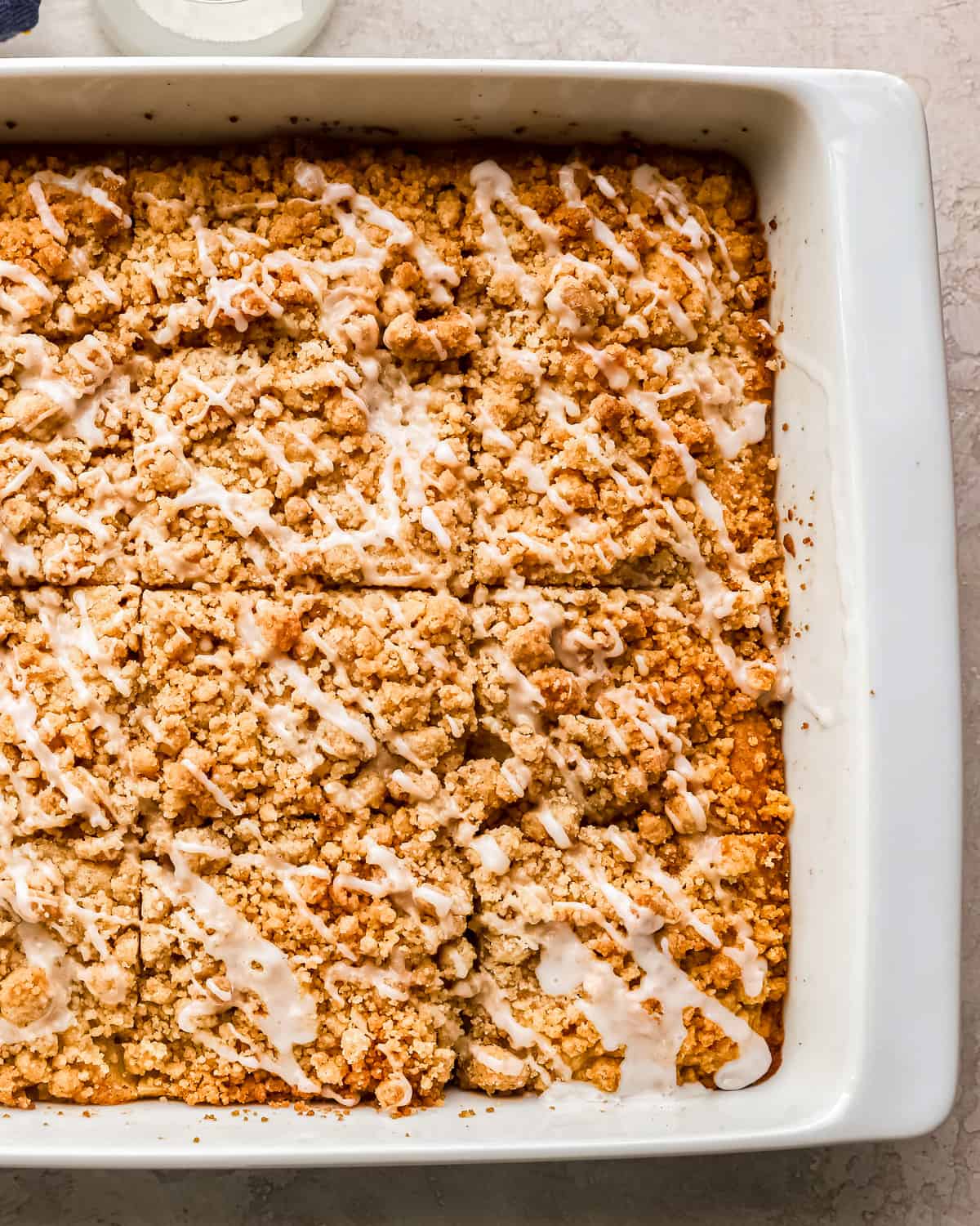 An apple coffee cake topped with streusel and a glaze, cut into squares.