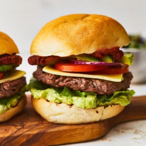 Two avocado burgers on a wooden cutting board.