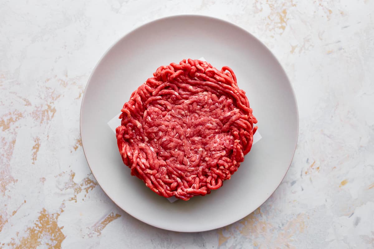 uncooked beef patty on a white plate.