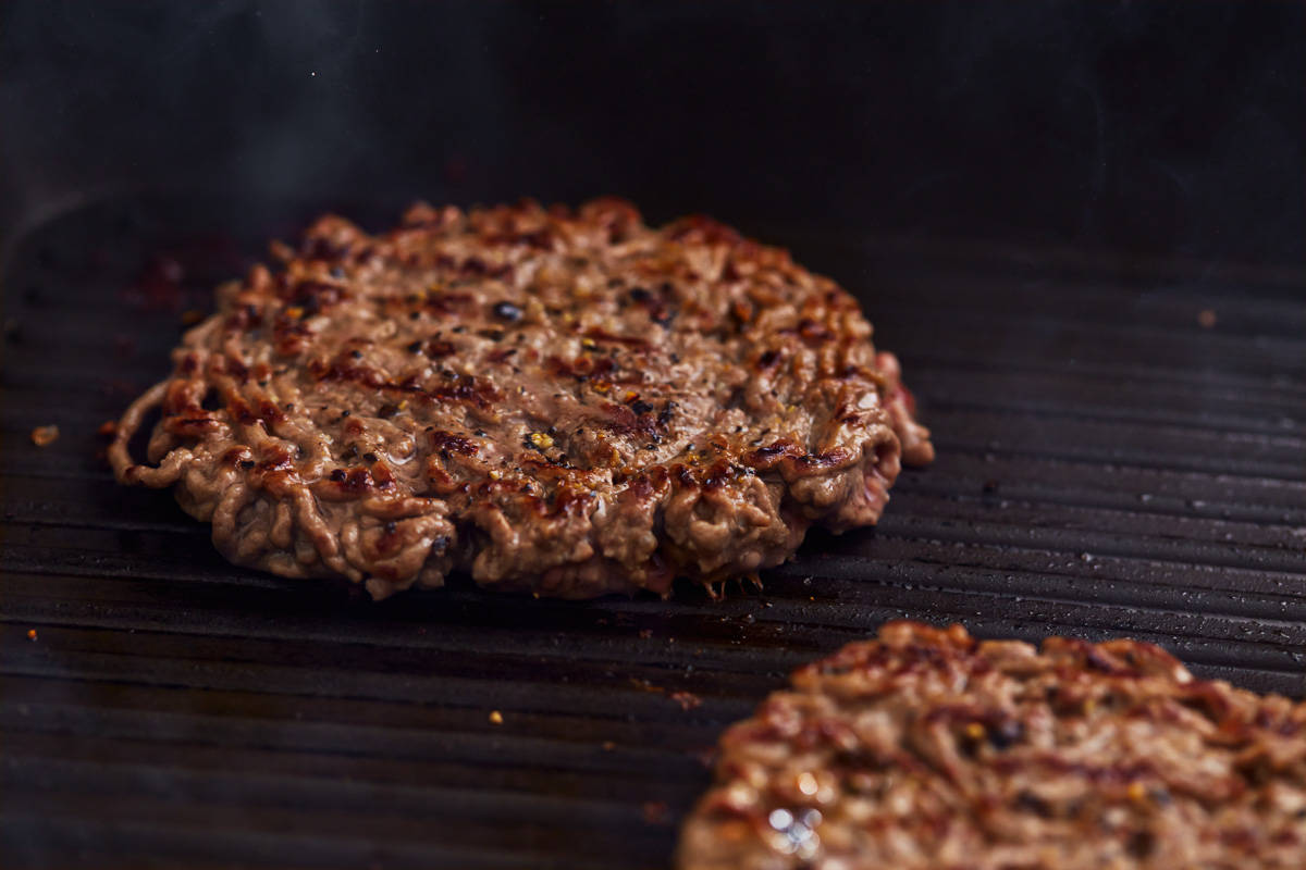 Two beef burger patties are being cooked on a grill.