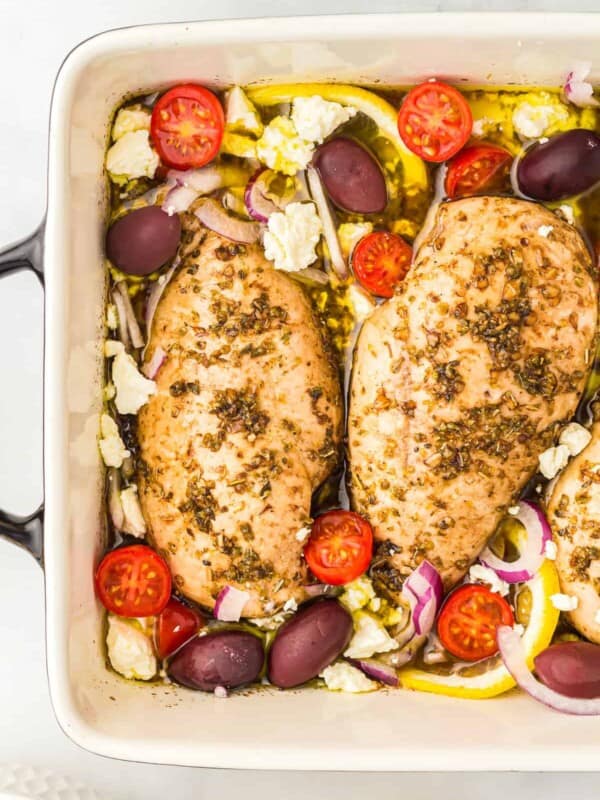 partial overhead view of baked greek chicken in a rectangular baking pan.