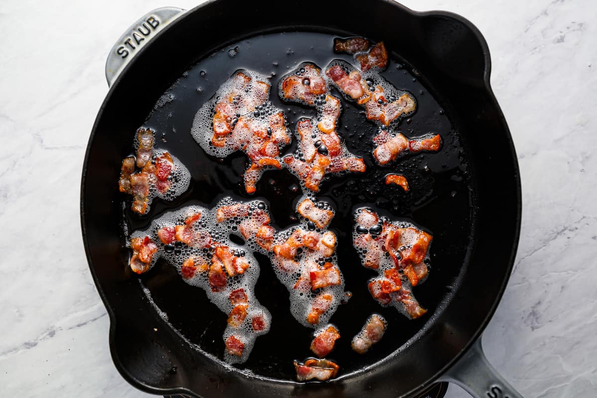Chopped pieces of bacon frying in a skillet.