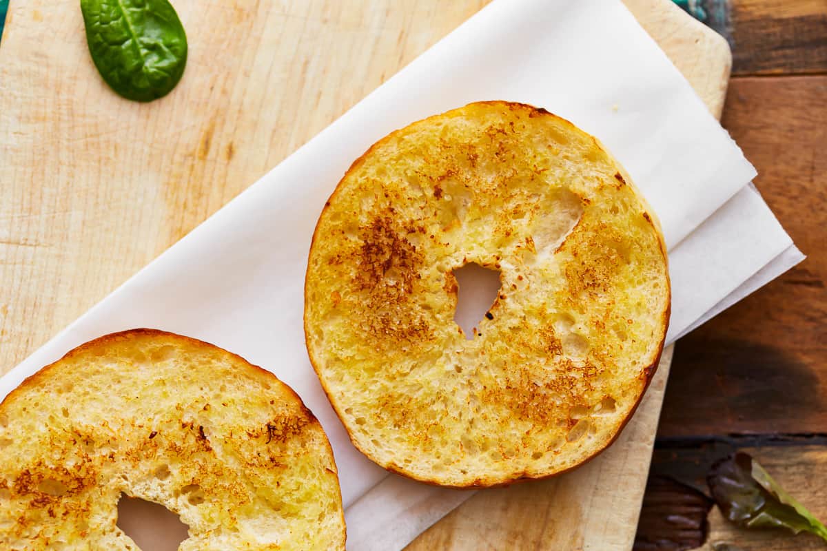 Two toasted bagel halves on a cutting board.