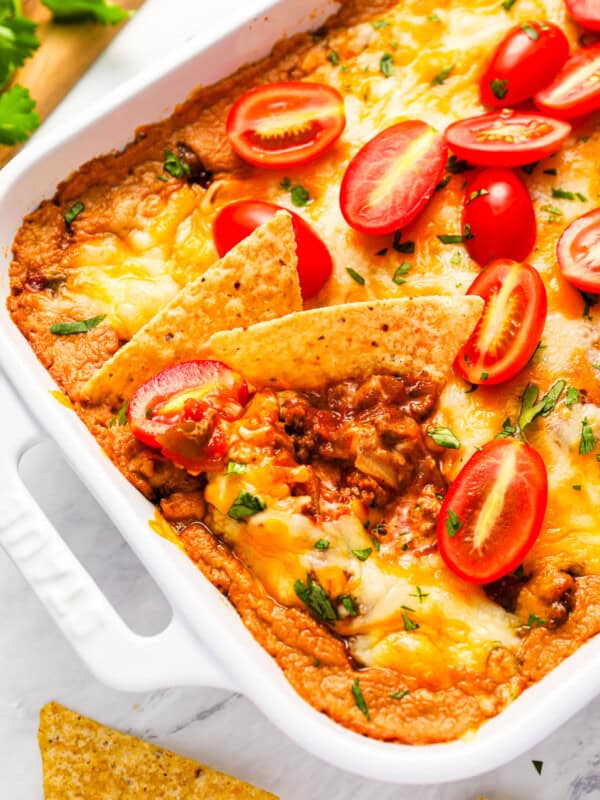 Mexican hot taco dip in a white dish with tomatoes and tortillas.