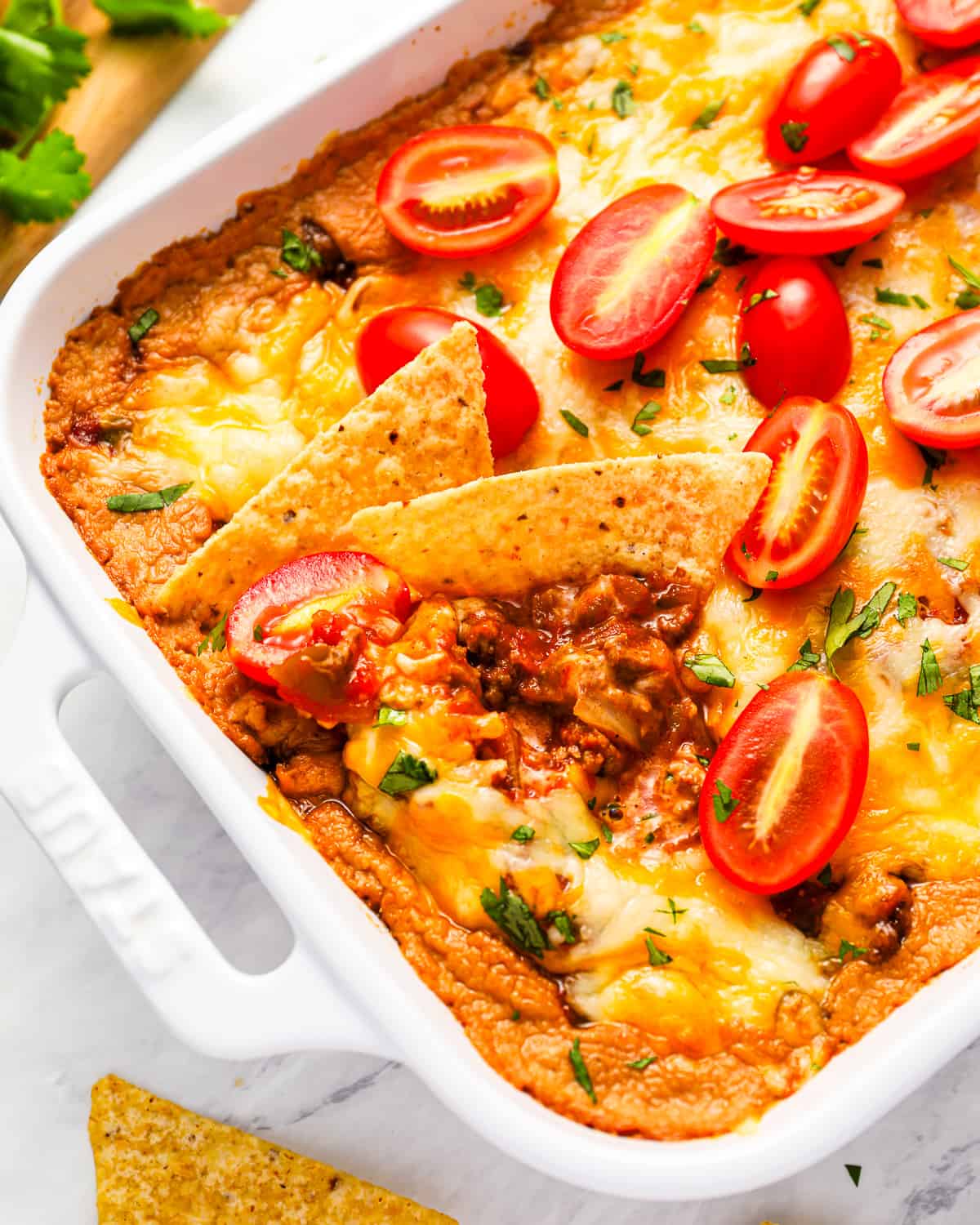 Mexican hot taco dip in a white dish with tomatoes and tortillas.