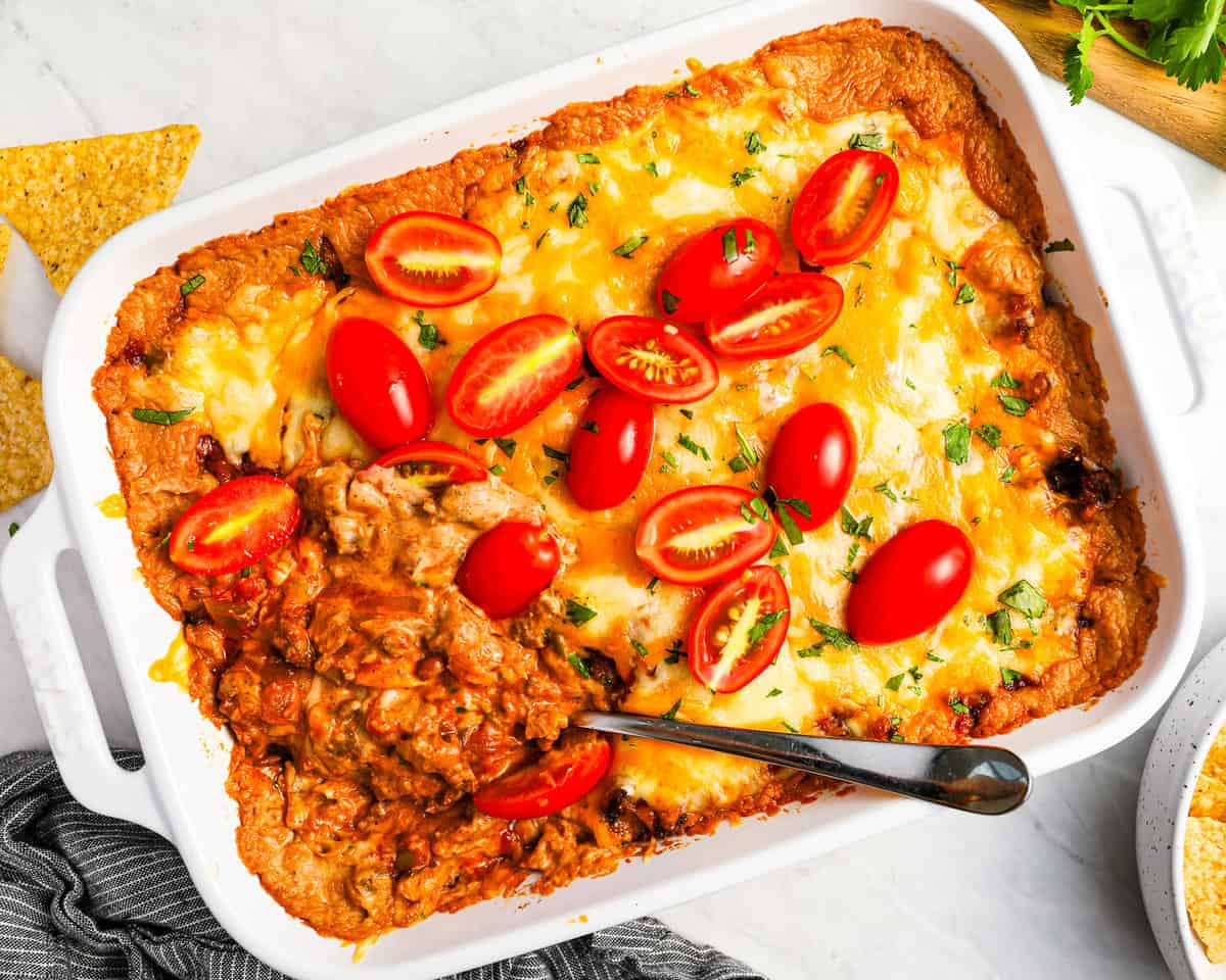 Hot cheesy mexican dip in a white dish with tomatoes and tortillas.