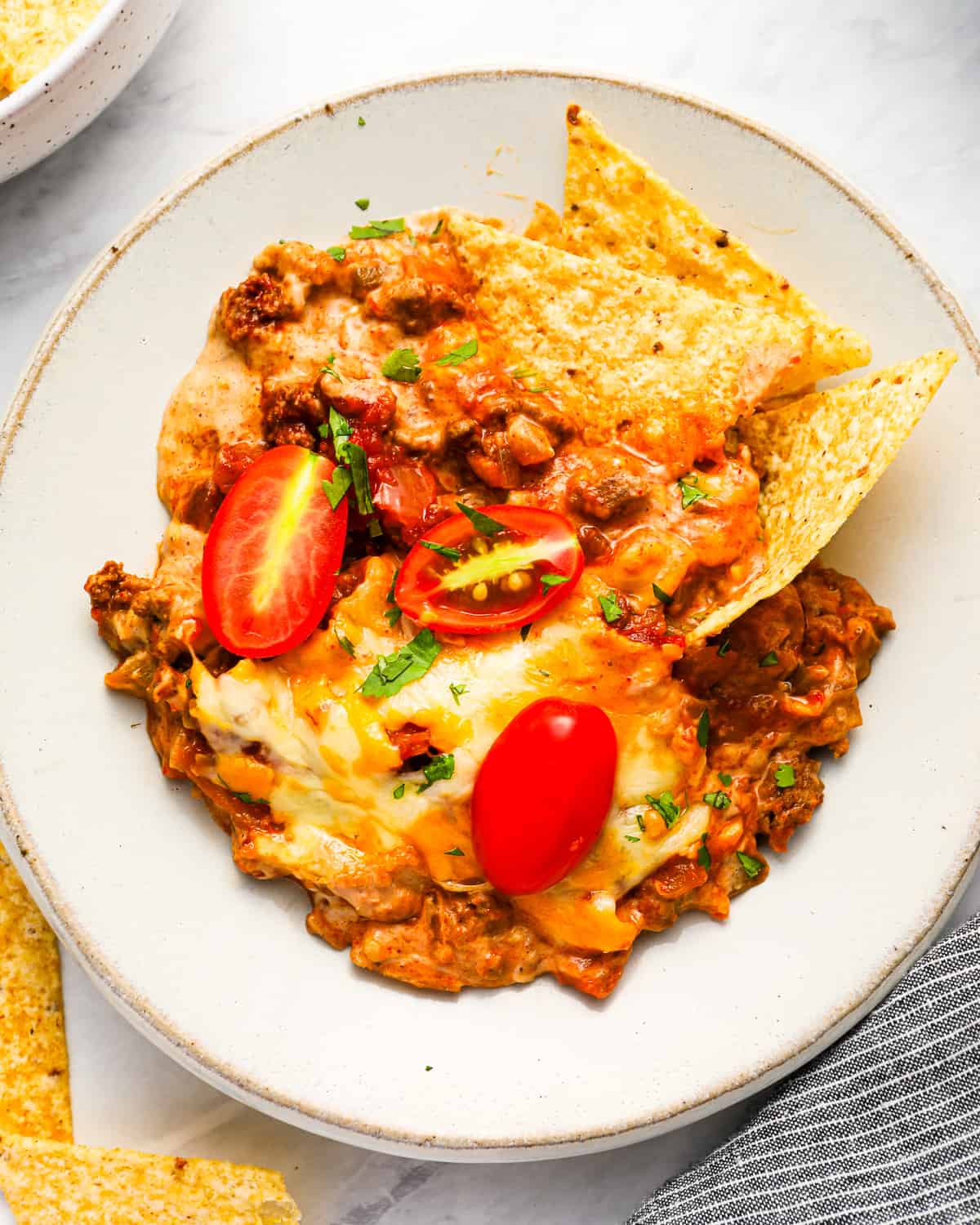 A plate of baked taco dip and tortilla chips, with ground beef, melted cheese, and fresh tomatoes.