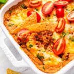 Mexican hot taco dip with tortilla chips and tomatoes in a white baking dish.