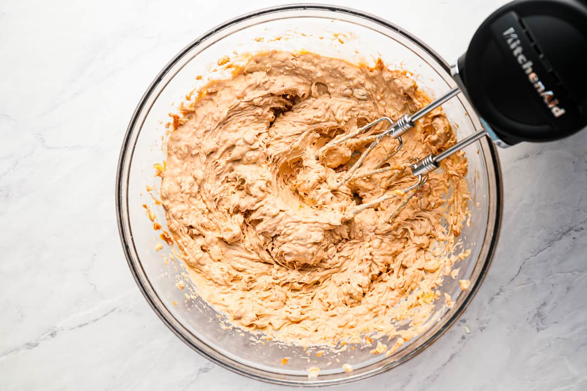 Blending a cream cheese mixture in a glass bowl with a handheld blender.