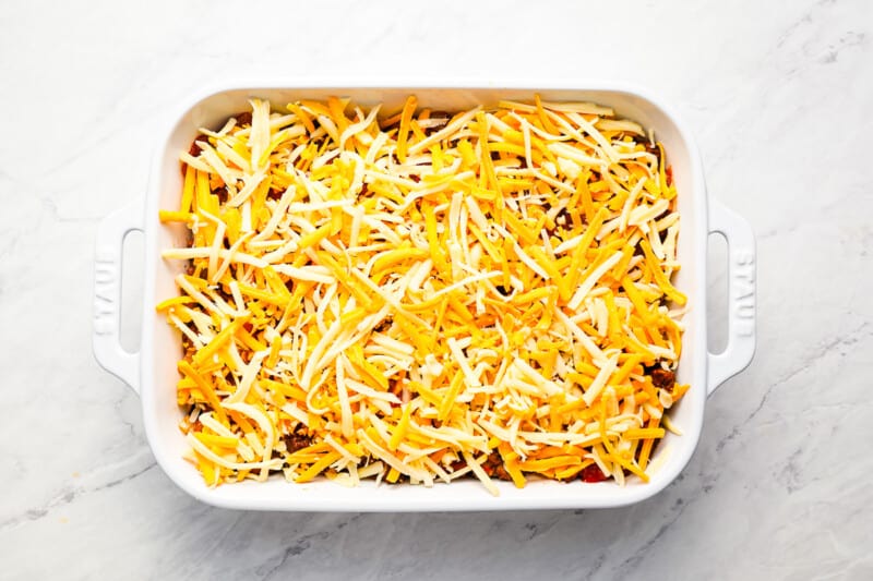 A hot taco dip with shredded cheese on top, served in a white casserole dish.