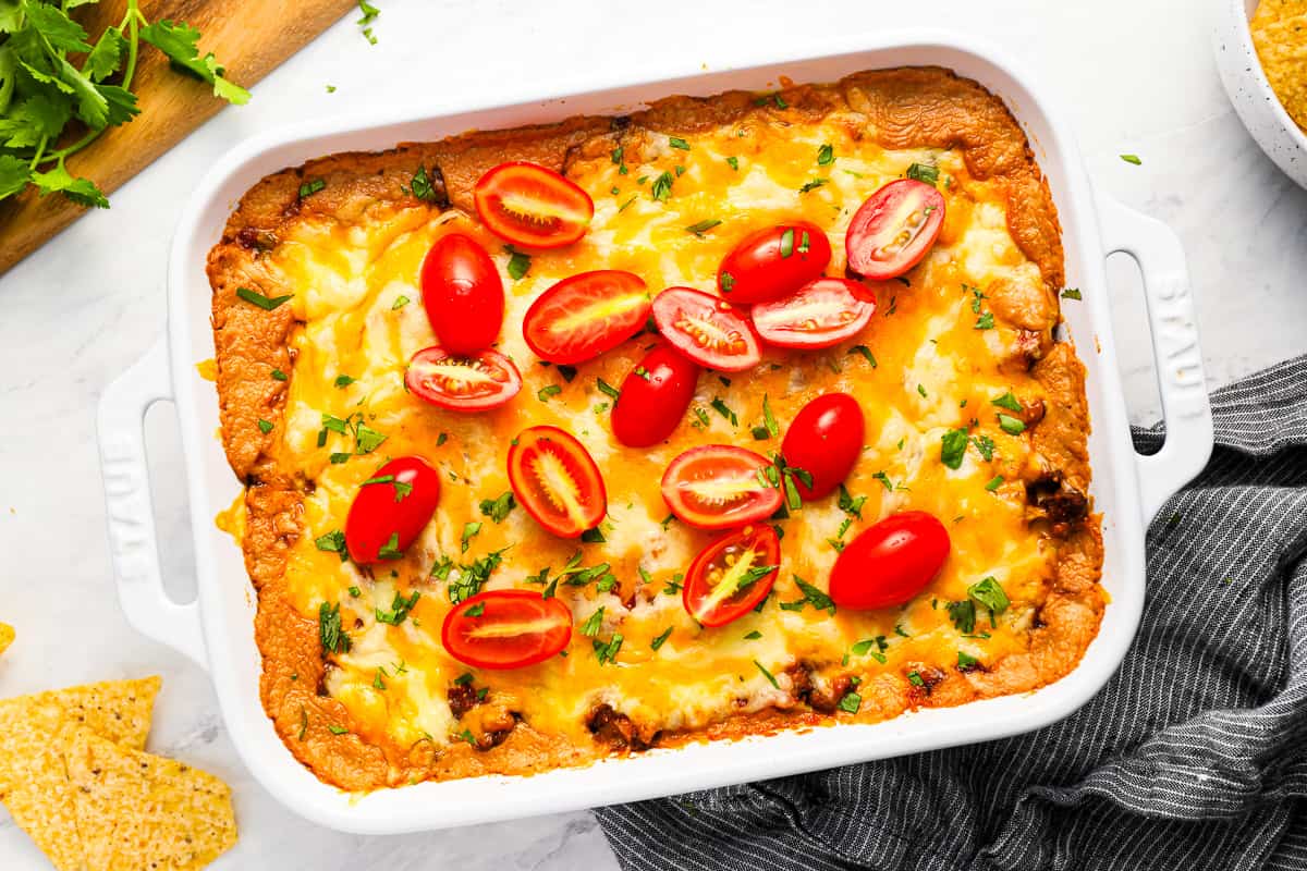 Hot taco dip in a white dish with tomatoes and tortillas.