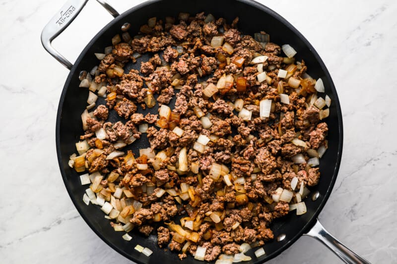 A sizzling skillet of hot taco dip, combining ground beef and onions.