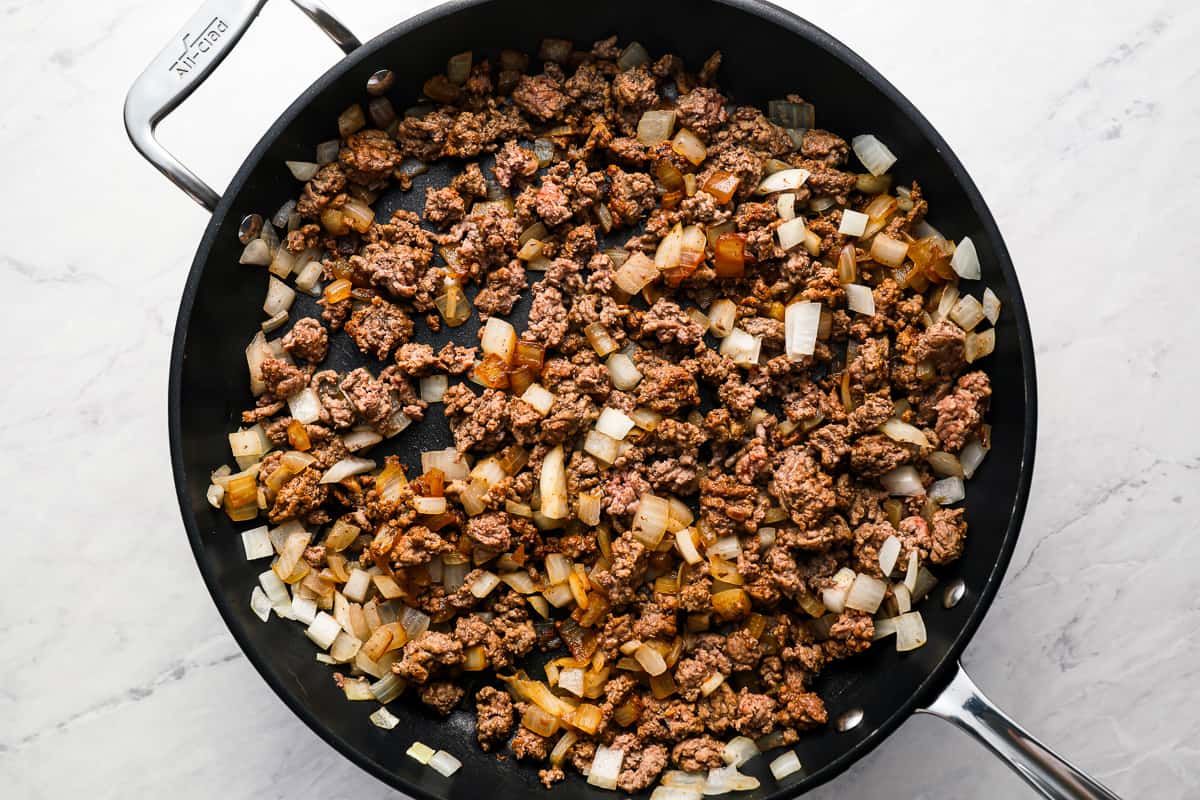 Ground beef and diced onions cooking in a skillet.