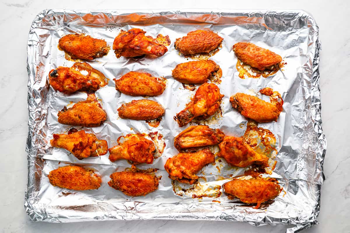 A sheet of aluminum foil with baked bbq chicken wings on it.