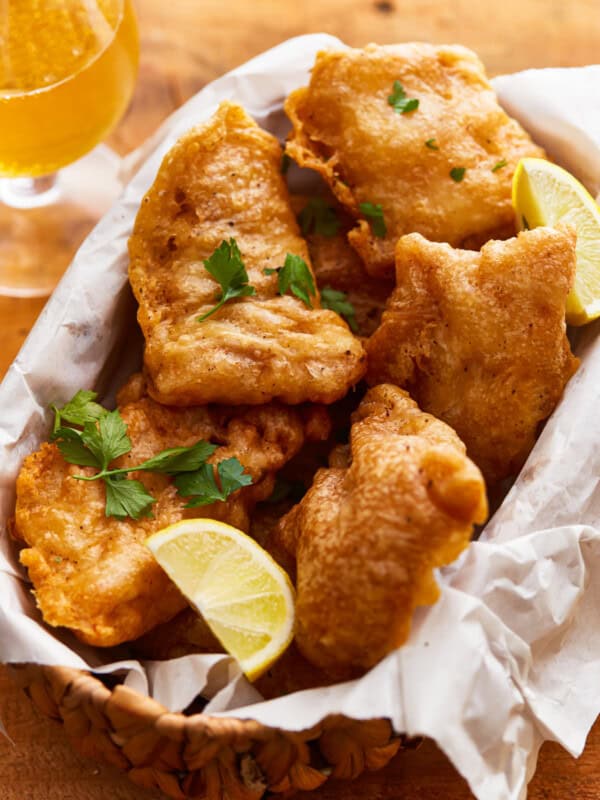 Beer battered fish in a basket with lemon wedges.