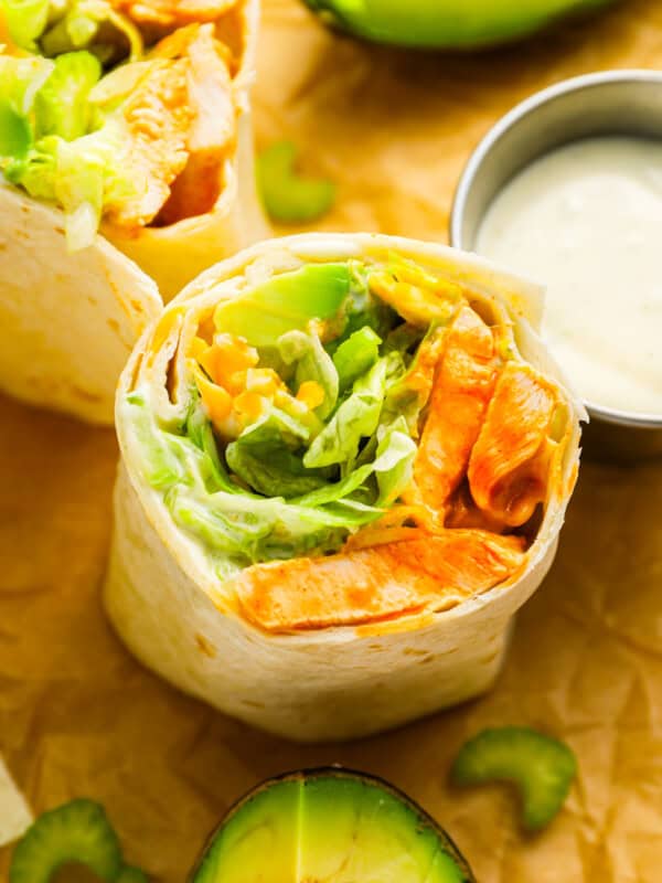 A buffalo chicken wrap with avocado on top of a piece of paper.