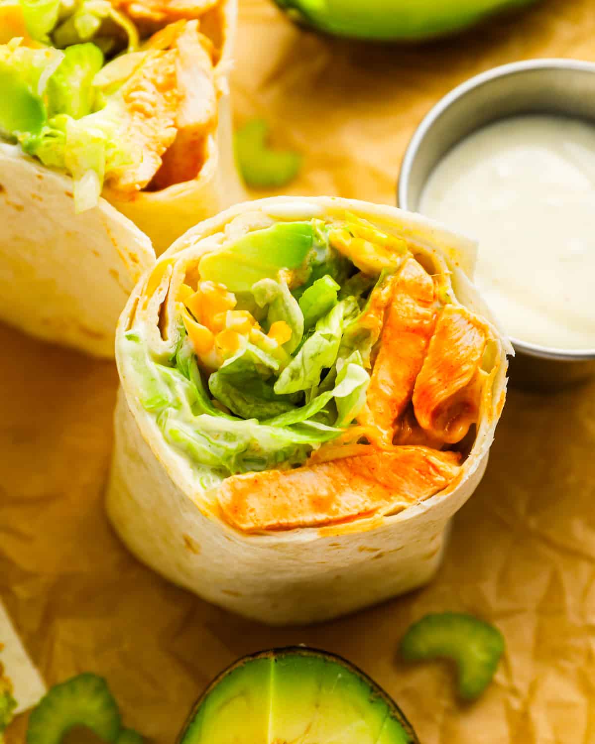 A buffalo chicken wrap with avocado on top of a piece of paper.