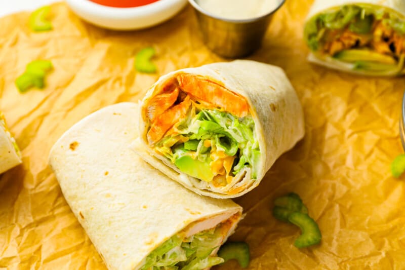 A buffalo chicken wrap with vegetables and sauce on a piece of paper.