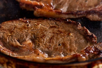 Two steaks are being cooked in a skillet.