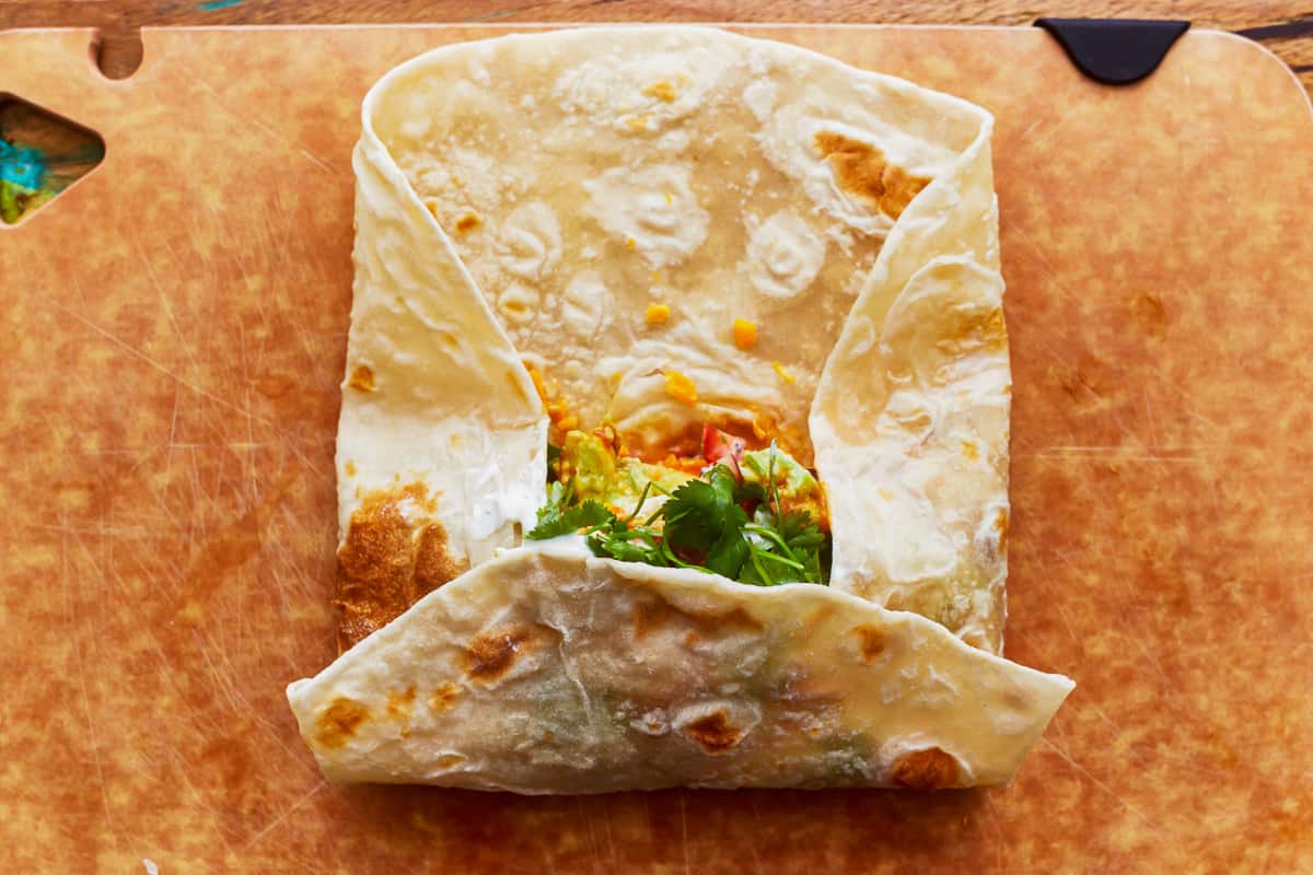 A partially rolled up California burrito on a cutting board.