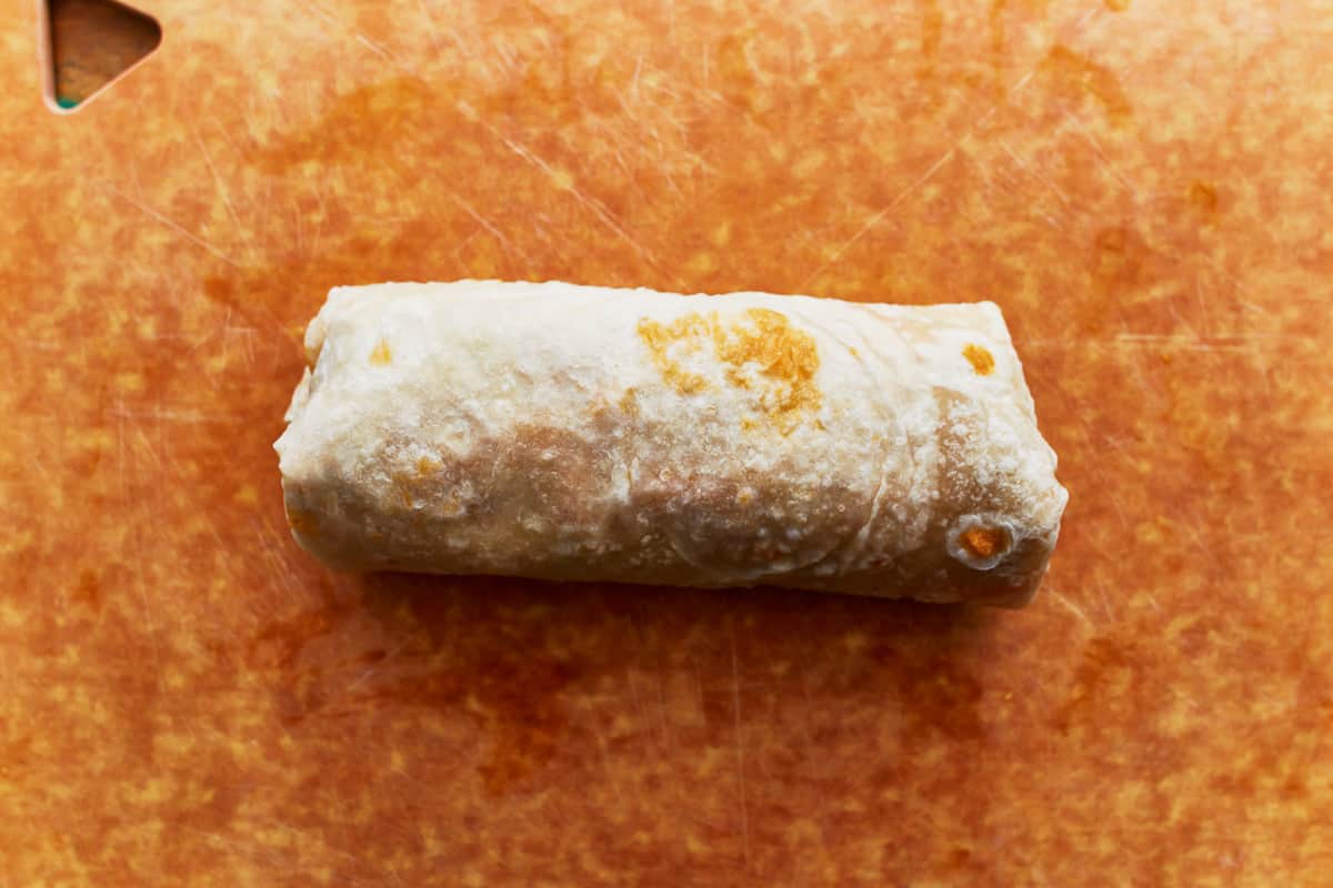 A rolled burrito on a cutting board.