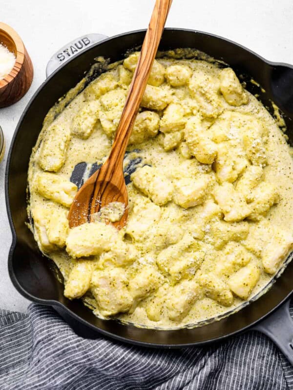 overhead view of gnocchi in pesto cream sauce in a cast iron skillet with a wooden spoon.