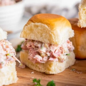 ham salad on slider rolls on a wooden cutting board.