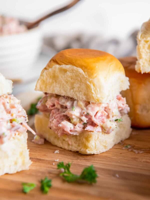 ham salad on slider rolls on a wooden cutting board.