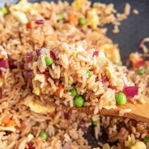 close up view of a wooden spoon lifting a scoop of vegetable fried rice from a wok.