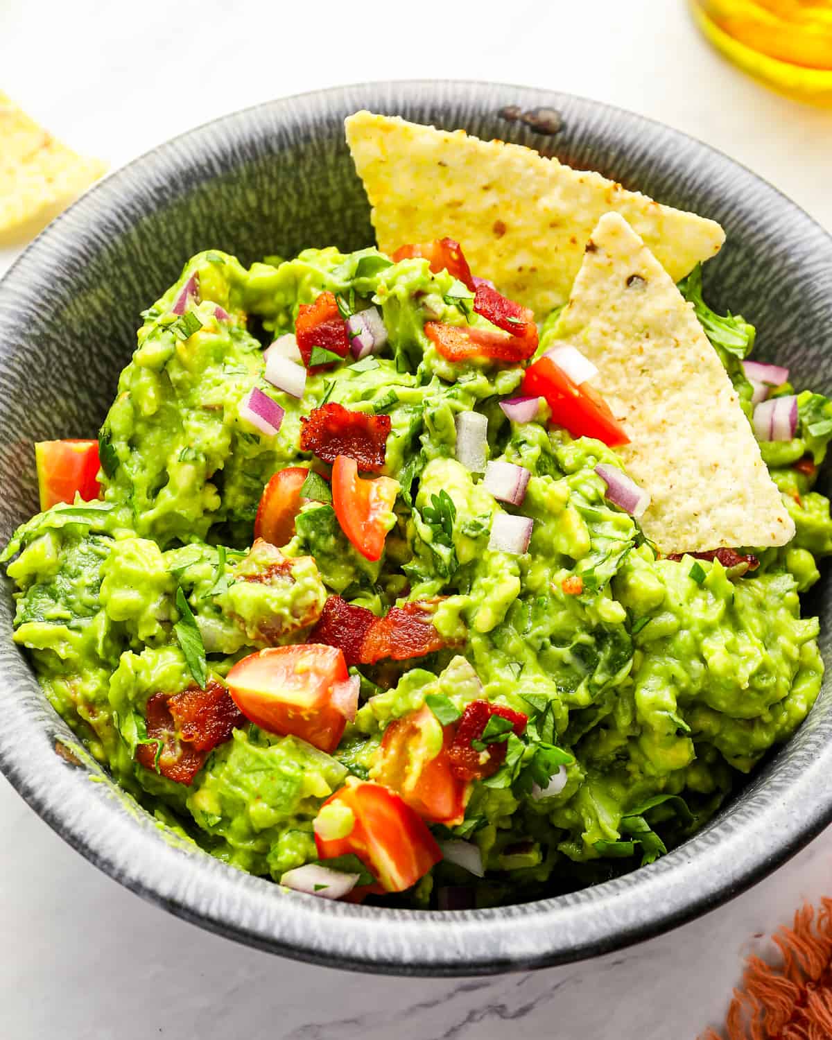 close up of blt guacamole in a bowl with tortilla chips.