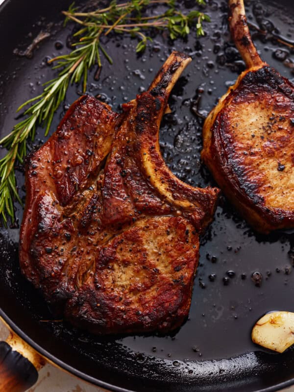 overhead view of seared bone in pork chops in a cast iron pan with herbs and garlic.