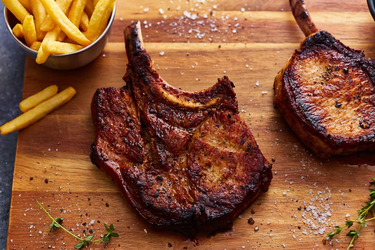 overhead view of seared bone in pork chops on a wooden cutting board with french fries.