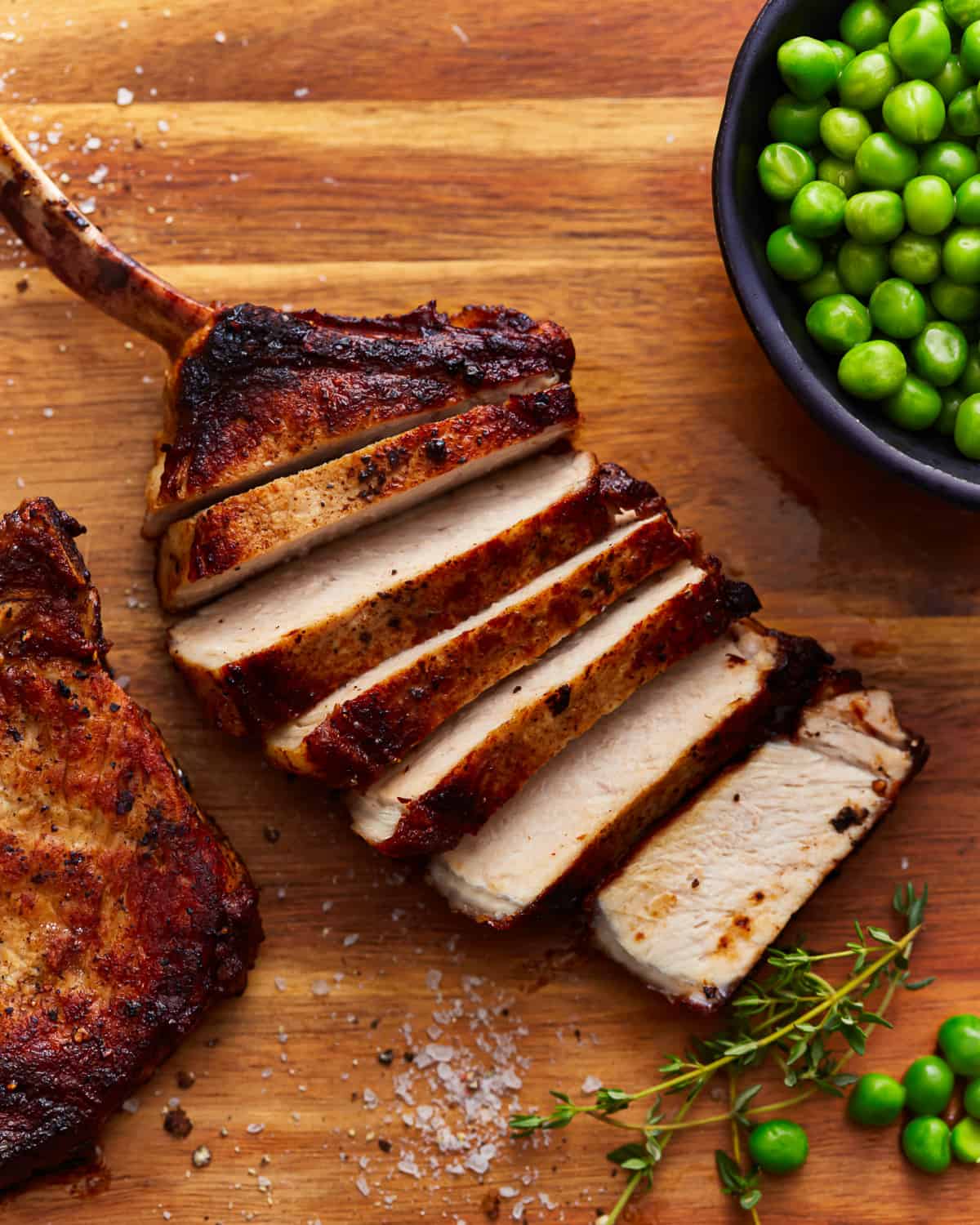 overhead view of a sliced pork chop on a wooden cutting board with peas.