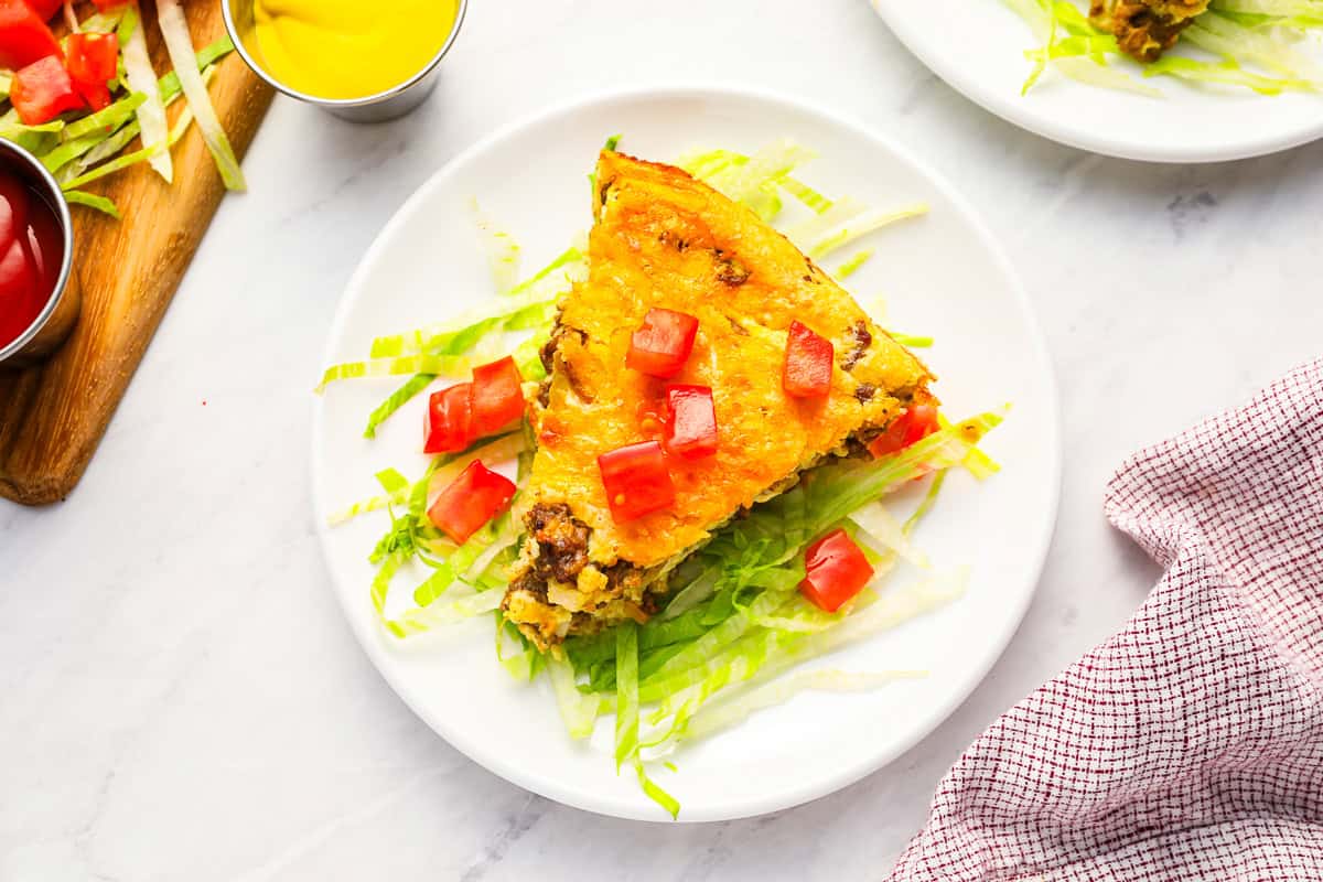 a slice of cheeseburger pie on a bed of lettuce and tomatoes on a white plate.