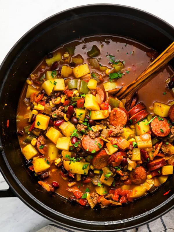 overhead view of cowboy stew in a dutch oven with a wooden spoon.