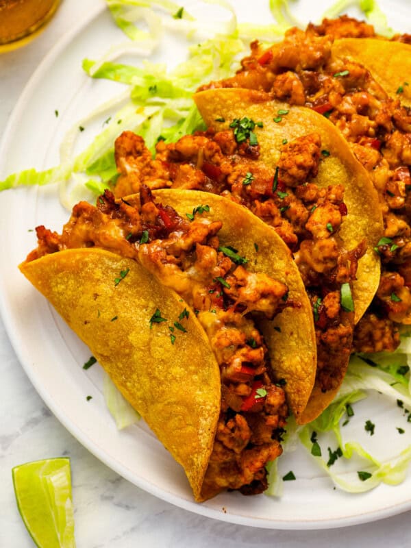 close-up view of 4 crispy chicken tacos on a white plate.