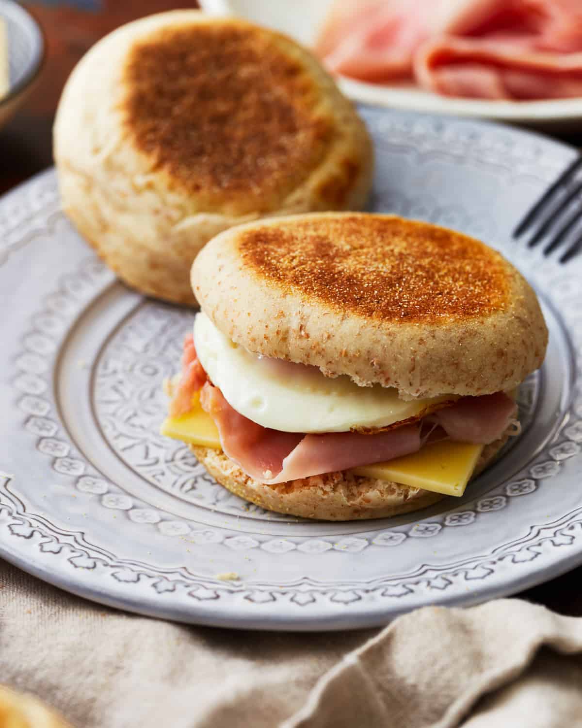 an egg sandwich on an english muffin on a white plate.