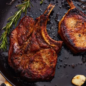 overhead view of seared bone in pork chops in a cast iron pan with herbs and garlic.