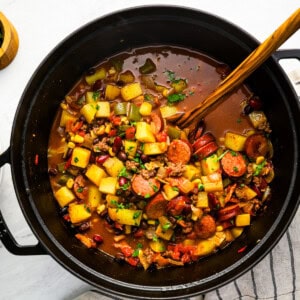 overhead view of cowboy stew in a dutch oven with a wooden spoon.