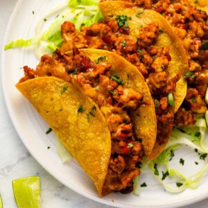 close-up view of 4 crispy chicken tacos on a white plate.