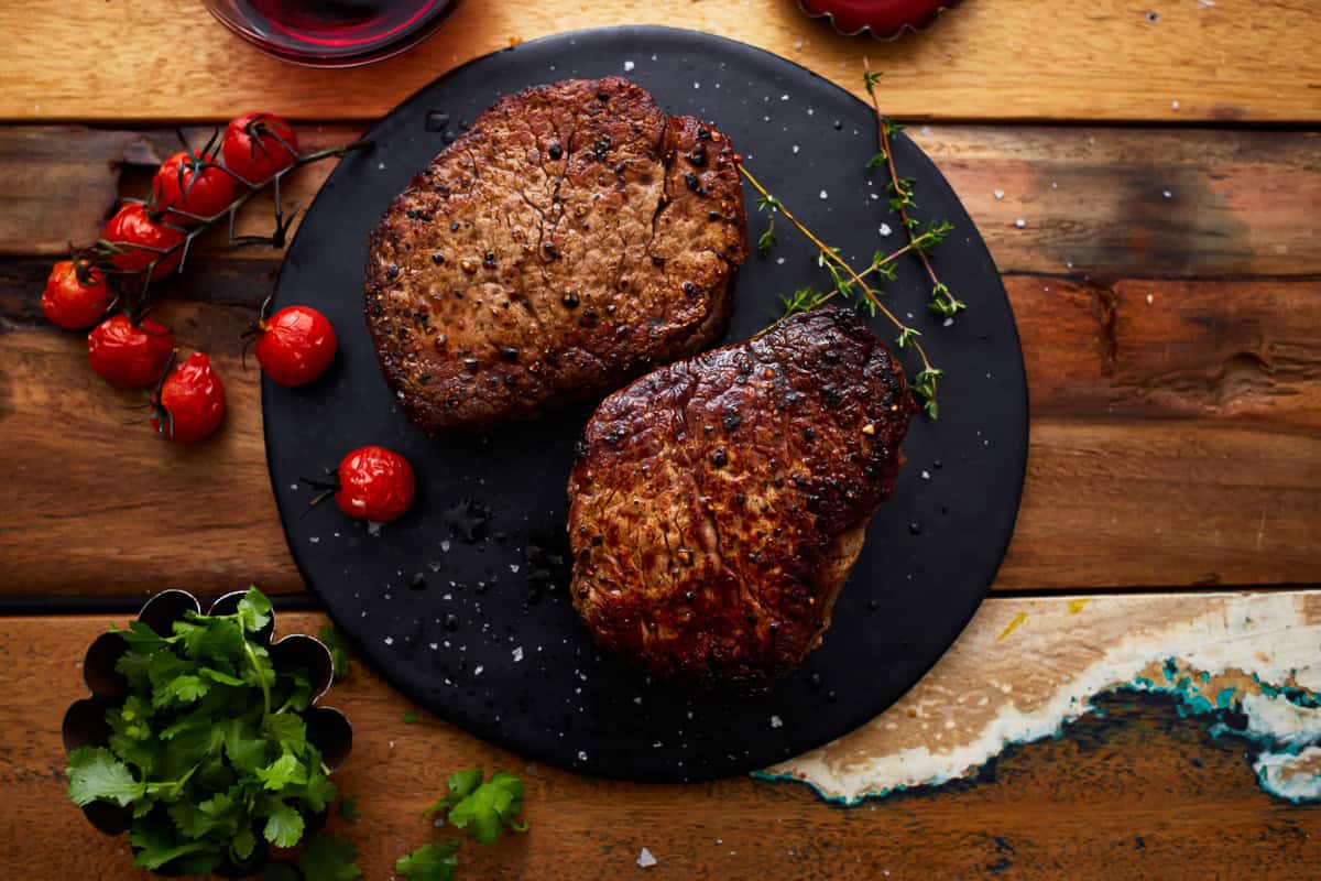 overhead view of 2 filet mignon on a black plate.