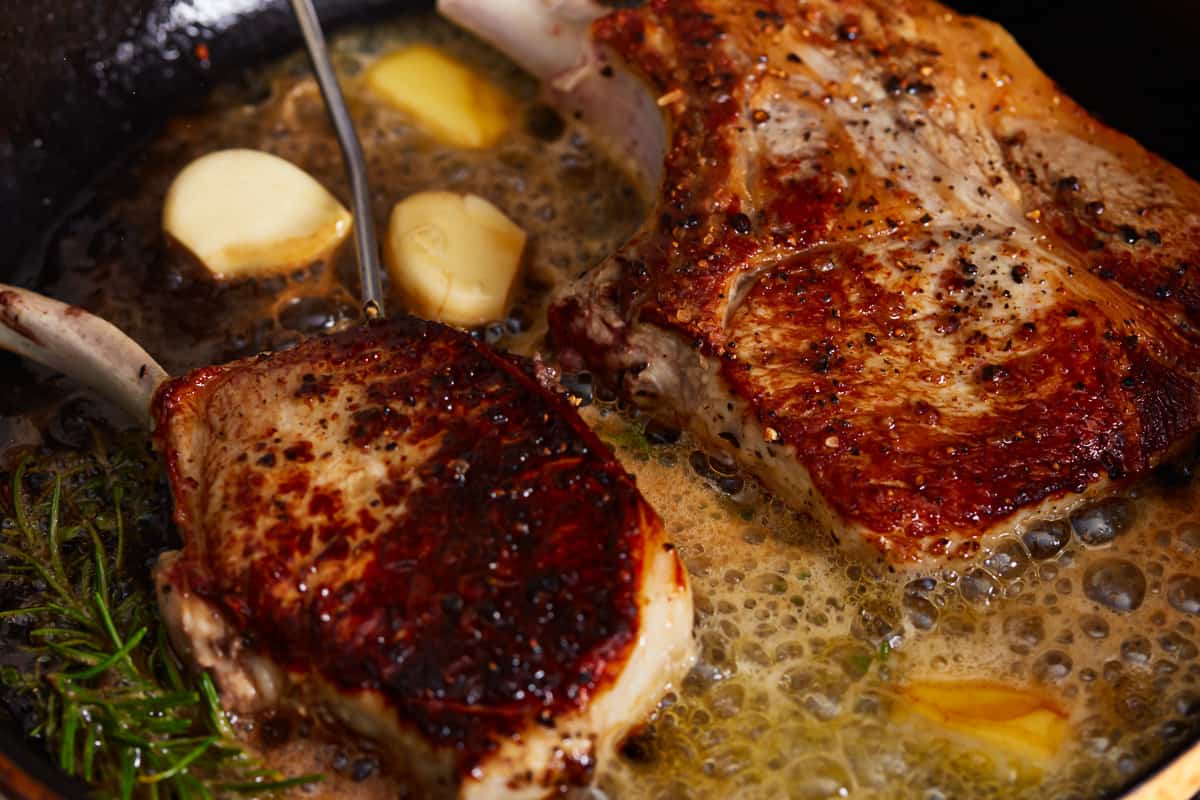 bone in pork chops searing in butter with garlic and herbs.